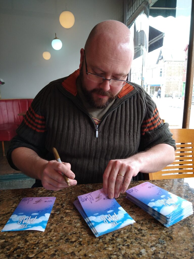 P.G. Bell signs bookplates for The Mab in a Cardiff coffee shop