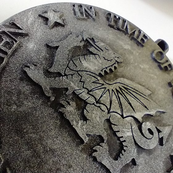 A circular stone medallion with a Welsh dragon design in the centre. The words "In Time of Need" are etched around the top.