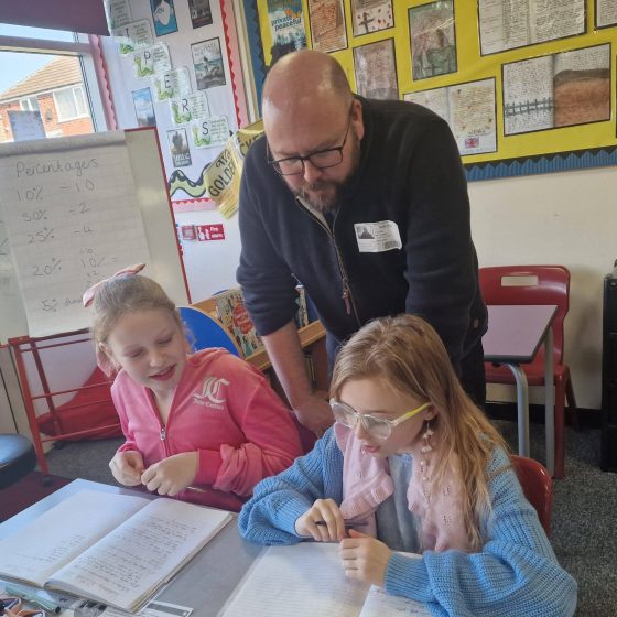 P.G. Bell leans over two female pupils, reading the work they've been doing in their exercise books.