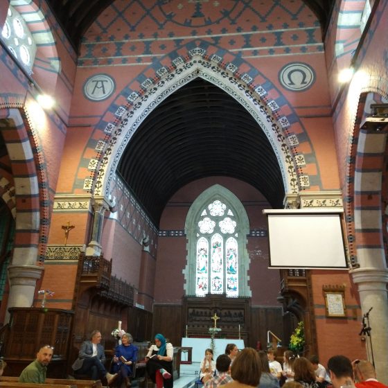 The interior of St Catherine's Church in Pontypridd. It is built in a neo-gothic style and richly decorated with red, grey and white tiles. People sit in the pews facing three authors sitting in front of the choir stalls.